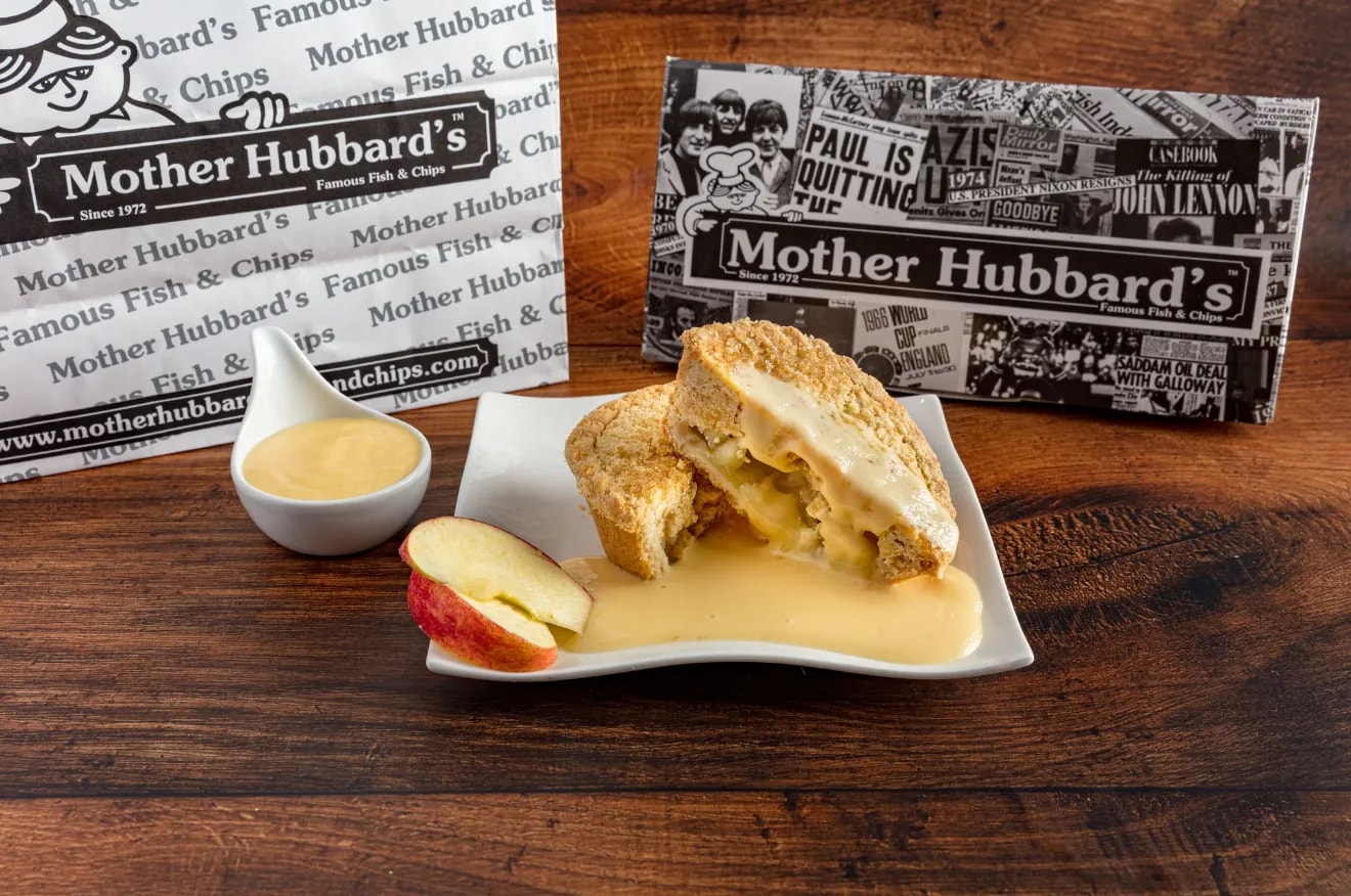 Apple crumble with custard on a square plate, with apple slices and a pot of custard