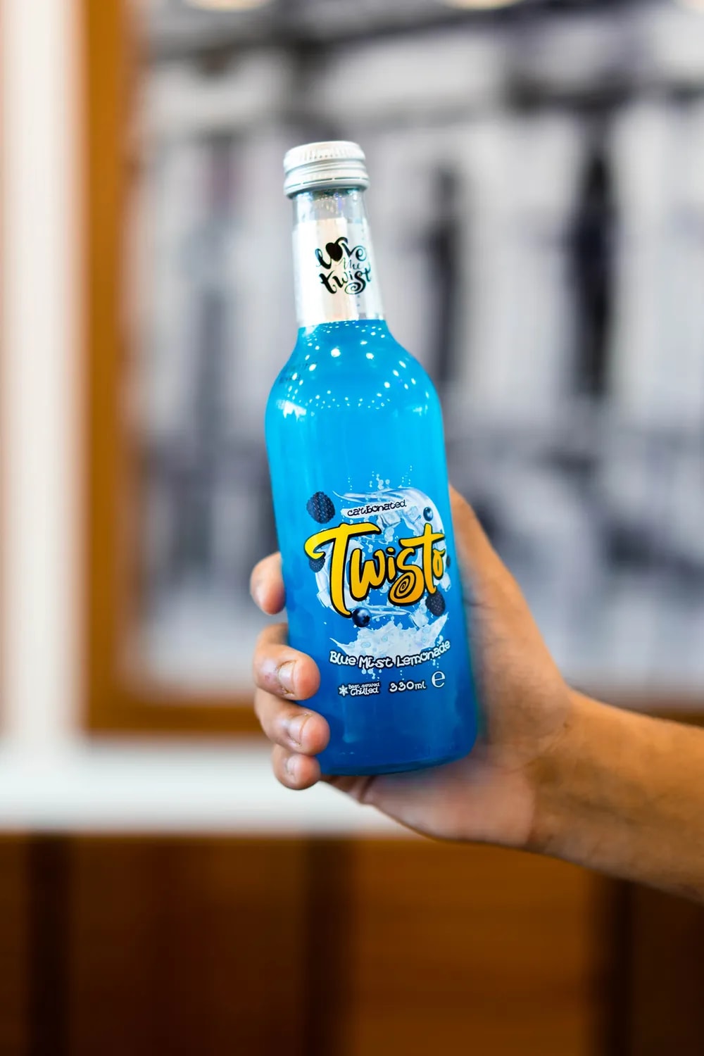 A hand holding a glass bottle of bright blue lemonade