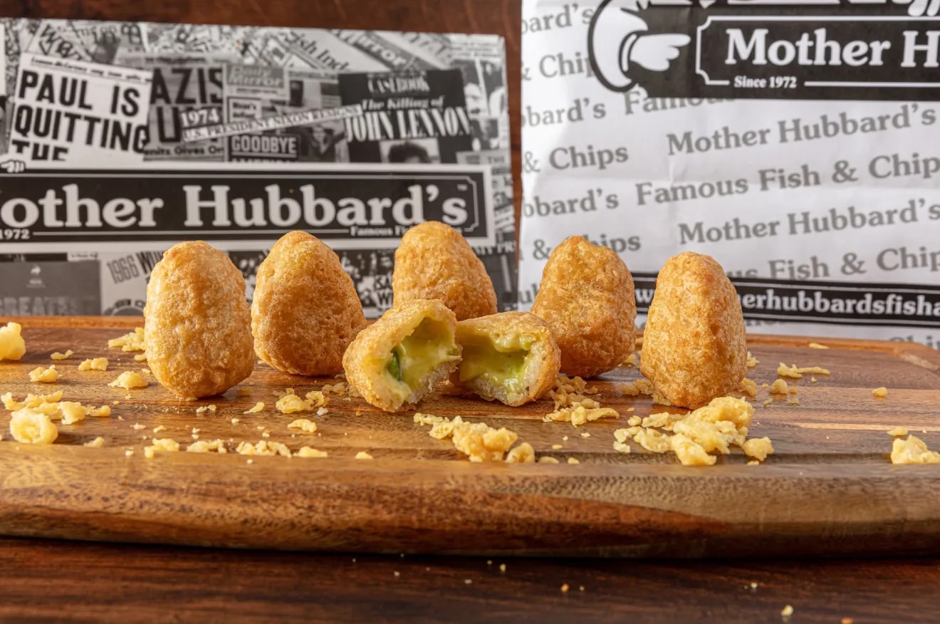 Breaded chilli cheese bites, one broken open, on a wooden board