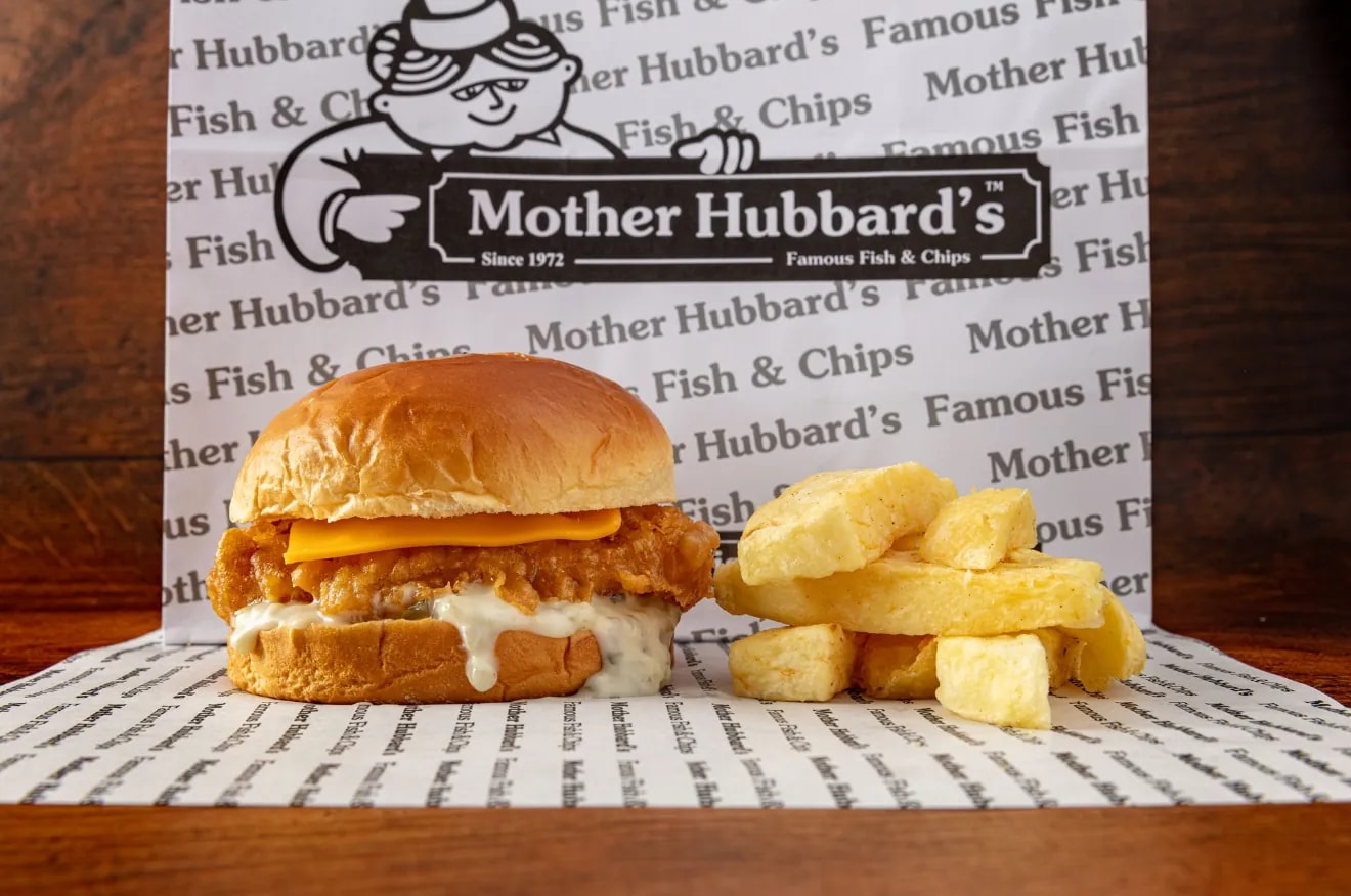 A crispy fish fillet sandwich with cheese and tartare in a brioche bun, beside chips