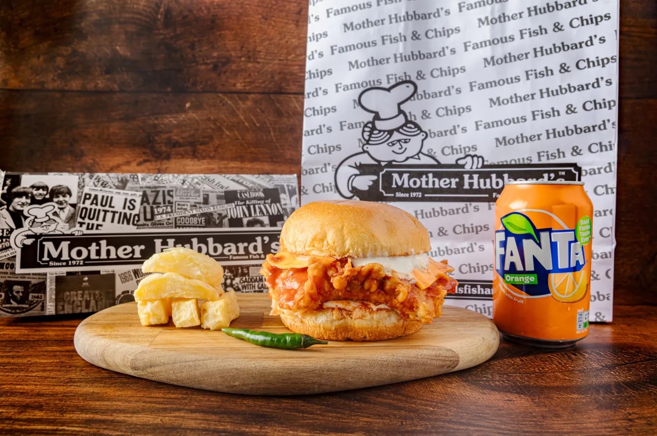 A dynamite fish sandwich in a brioche bun with chips, a green chilli and a can of Fanta