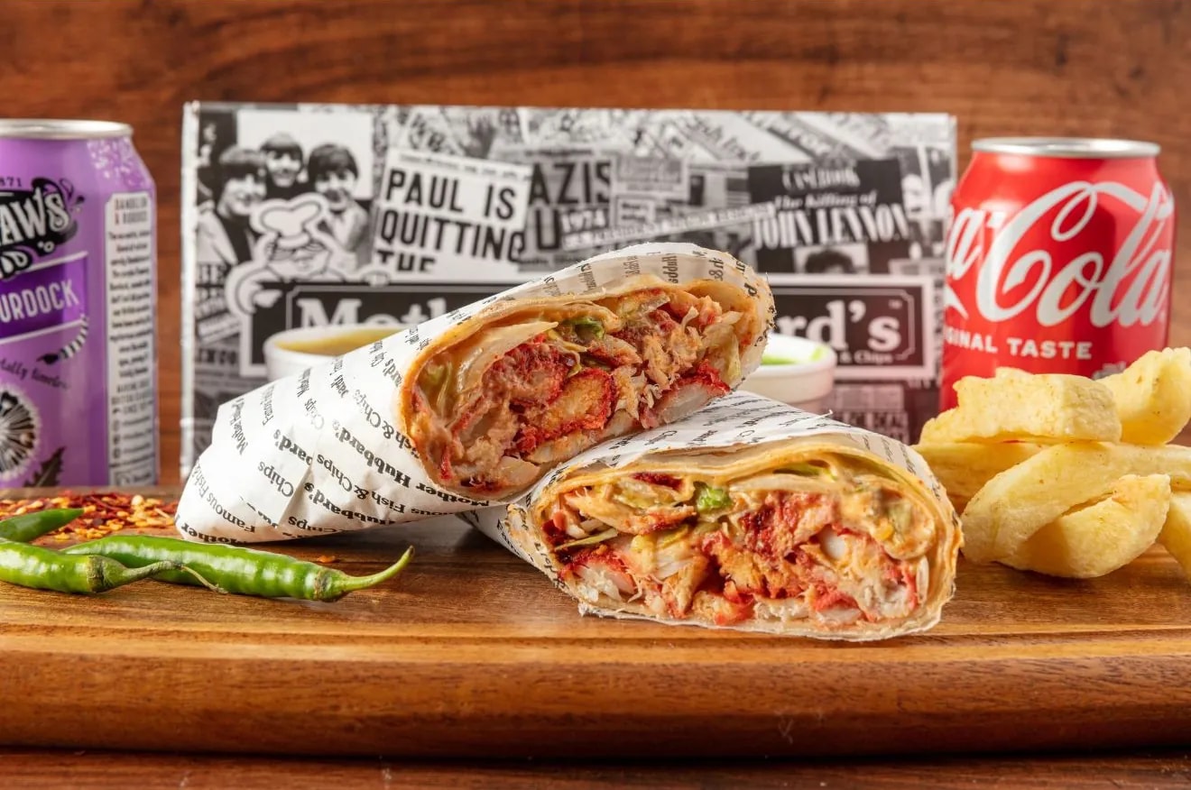 A fiery fish wrap cut in two, with green chillies and chips, between a can of Ben Shaw’s and a Coca-Cola