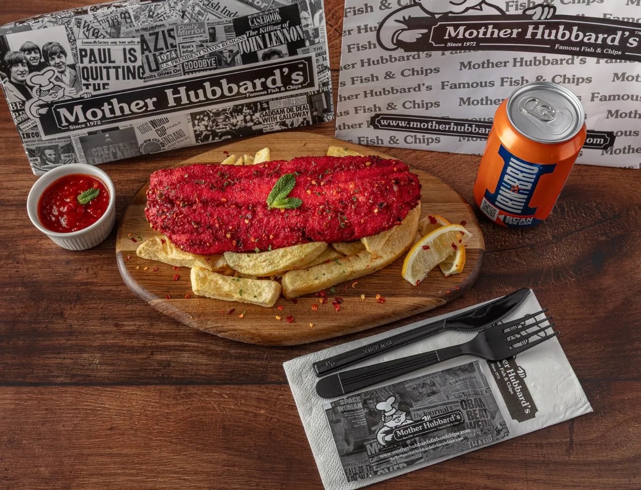 Fish in a fiery red coating on a board of chips with a lemon wedge, a dip and a can of Irn-Bru