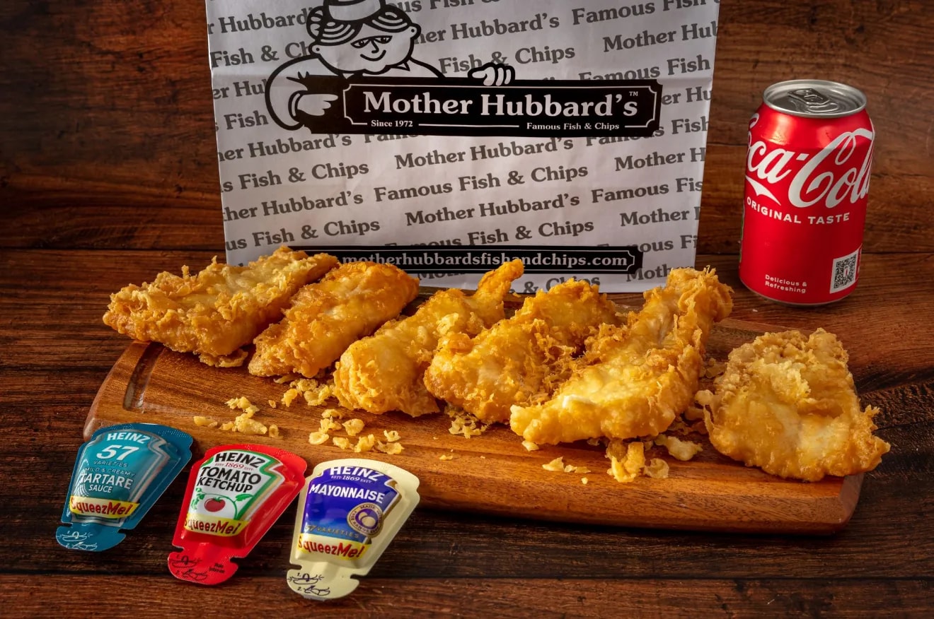 Golden fish bites on a wooden board with tartare, ketchup and mayonnaise sachets and a can of Coca-Cola