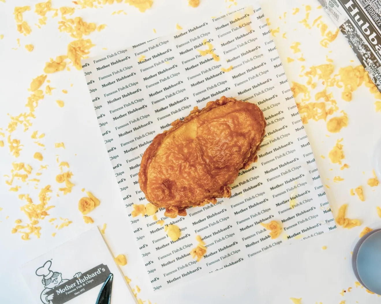 A golden battered fish cake on Mother Hubbard’s printed paper