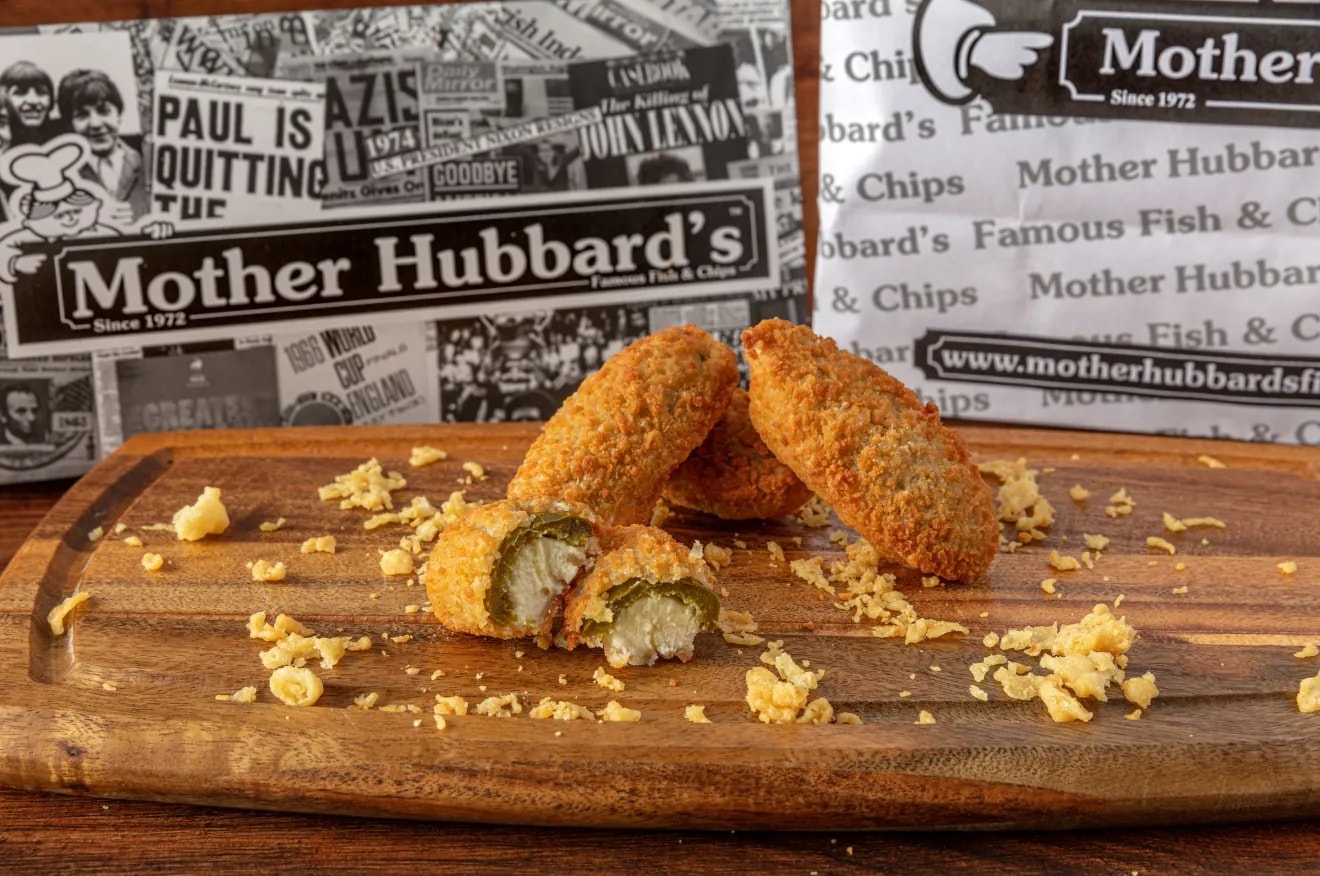 Breaded jalapeño cheese bites, one cut open to show the filling, on a wooden board