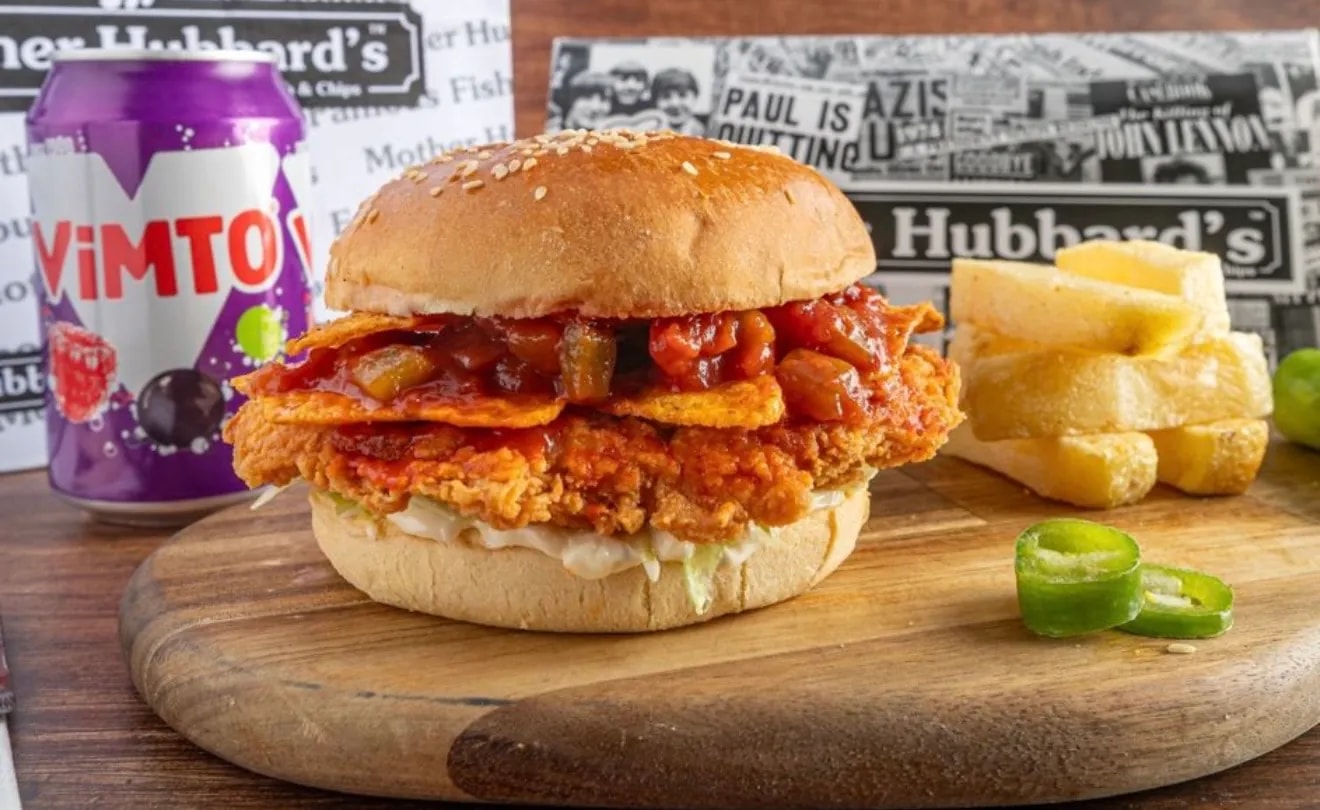 A crispy chicken sandwich with salsa and tortilla crisps in a sesame bun, beside chips