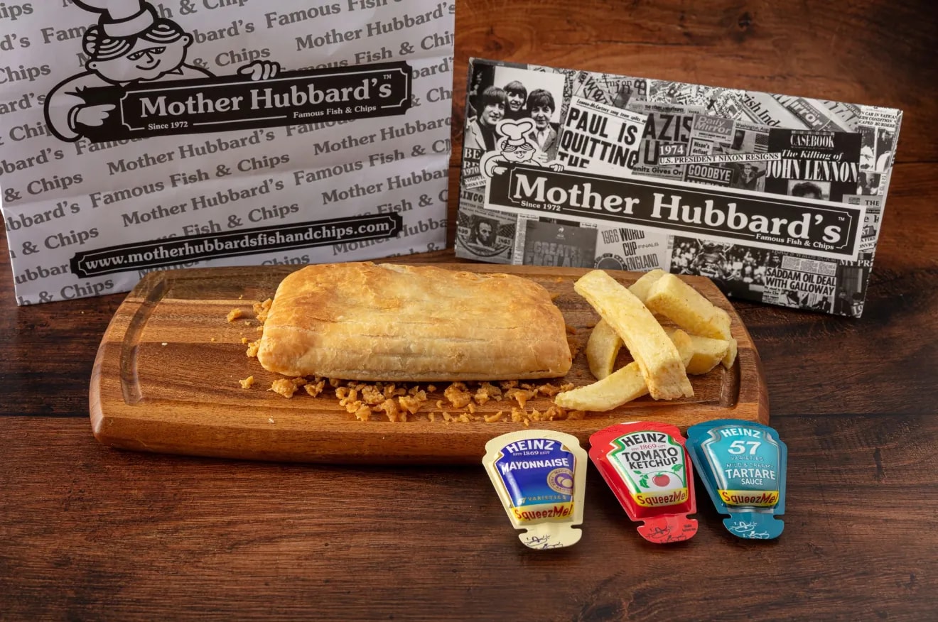 A peri pasty on a wooden board with chips and sauce sachets