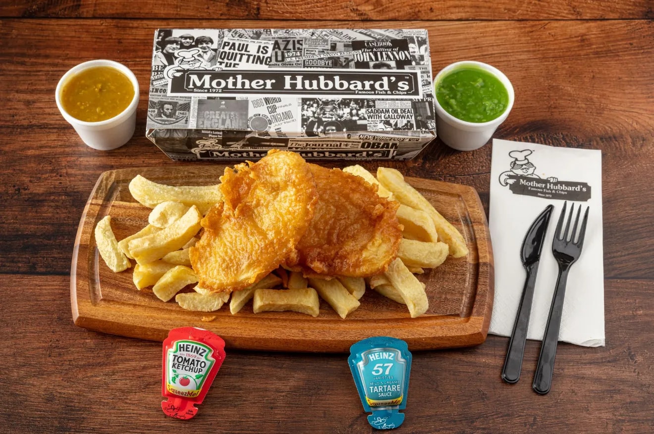 Battered potato scallops on a board of chips, with curry sauce, mushy peas and cutlery