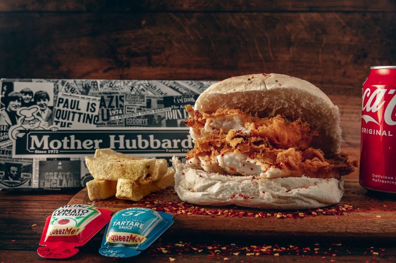 A spicy fish butty piled with crispy coated fish and chilli flakes, beside chips and a can of Coca-Cola