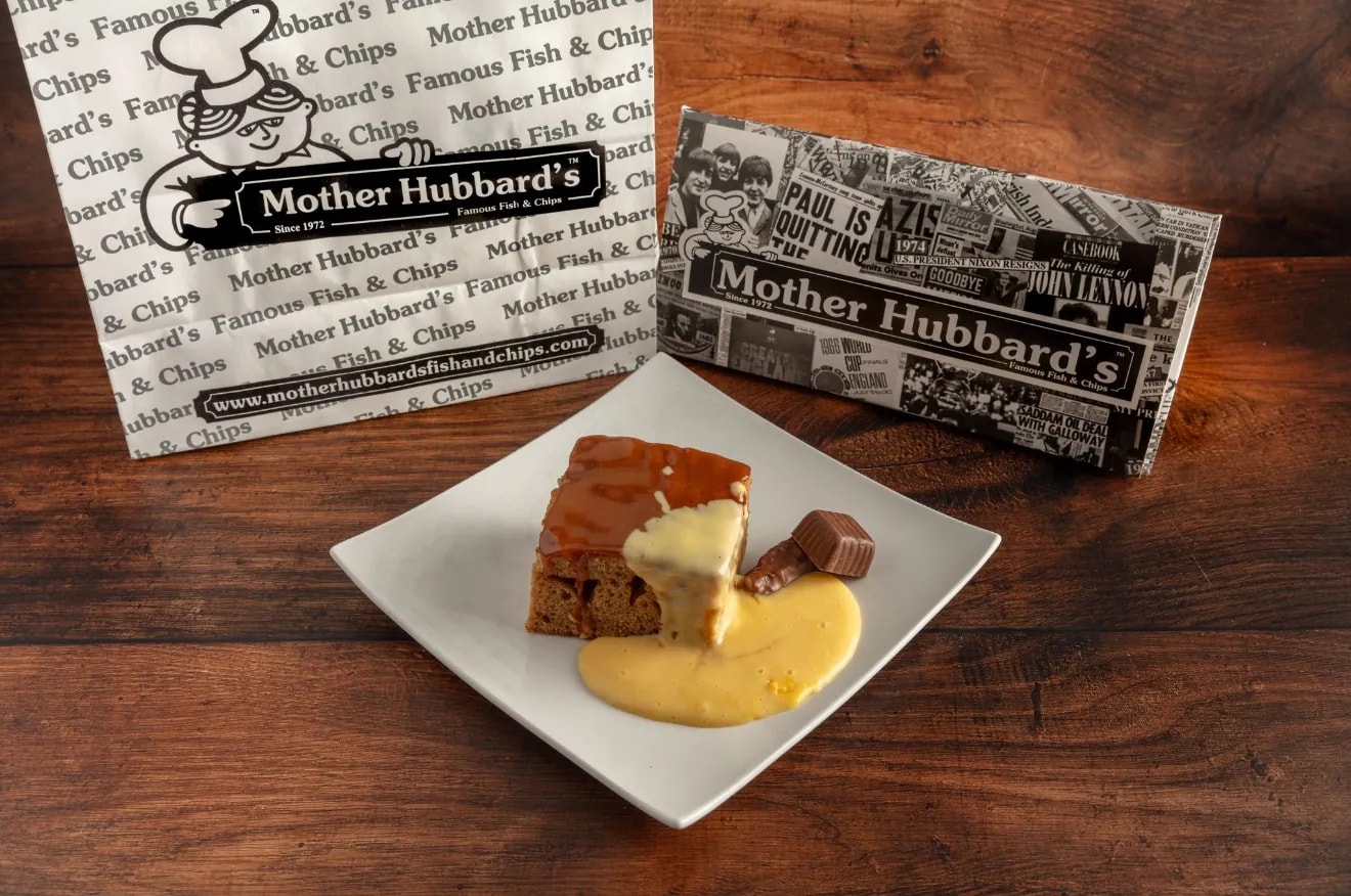 Sticky toffee pudding with custard and a toffee on a square plate